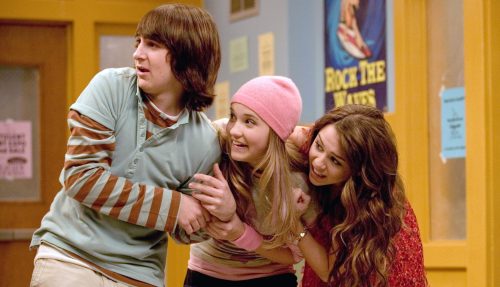 Miley Cyrus with Emily Osment and Mitchel Musso as their characters on Hannah Montana; the friends huddle and look off anxiously